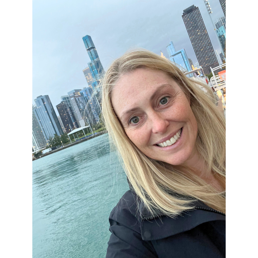 Woman smiling in front of a waterfront cityscape, with tall modern buildings in the background.