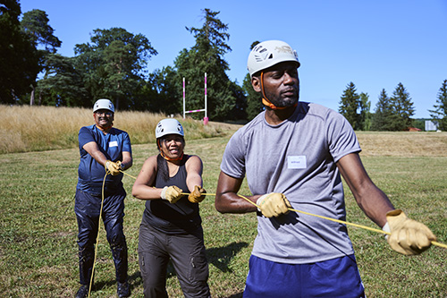 3 students wearing hard hats pulling on a rope 