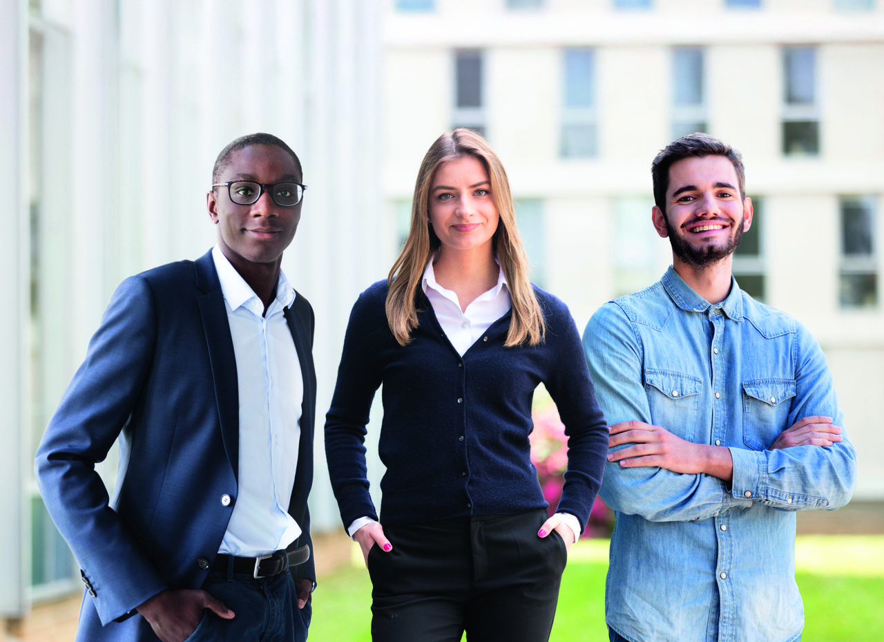 Three Masters students standing outside dressed casually and posing with smiles