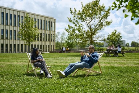 Two MBA students sitting on chairs and chatting on the lawn outside the MBA Building in Jouy-en-Josas