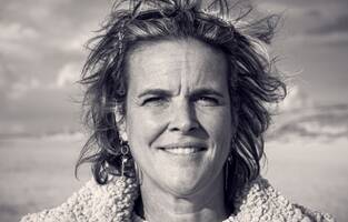 Black-and-white portrait of Frederique Veldhuis outdoors, facing the camera, wind in her hair, with an open landscape in the background.