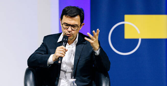 Rodolphe Durand, seated with a microphone, speaks and gestures during a panel discussion