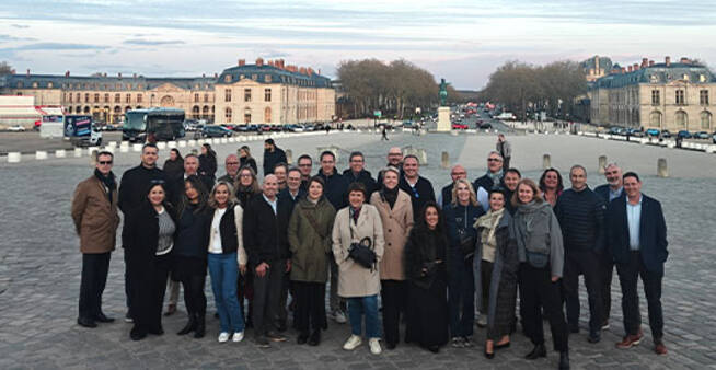 Around thirty participants pose as a group in front of the Château de Versailles.