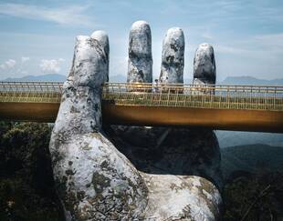 un homme marche sur un pont soutenu par un rocher en forme de main