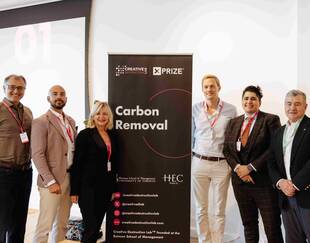 Group photo of six people standing next to a 'Carbon Removal' banner at a Creative Destruction Lab XPRIZE event. The individuals are smiling and wearing business attire with name badges. The banner includes logos from the Rotman School of Management at the University of Toronto and HEC Paris.