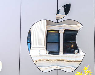 A reflective Apple logo on a building facade, distorting the reflection of classical architecture in its polished surface.