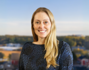 Woman smiling in front of a blurred cityscape, wearing a dark patterned blouse.