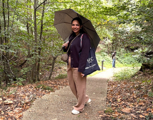 MBA Participant Aayushee Shukla standing in the forest of HEC Paris with an umbrella