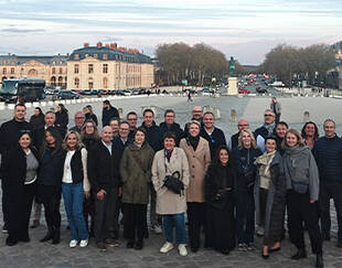 Around thirty participants pose as a group in front of the Château de Versailles.