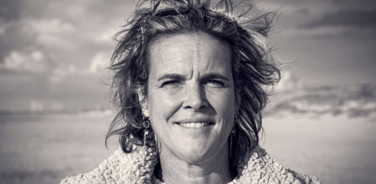 Black-and-white portrait of Frederique Veldhuis outdoors, facing the camera, wind in her hair, with an open landscape in the background.