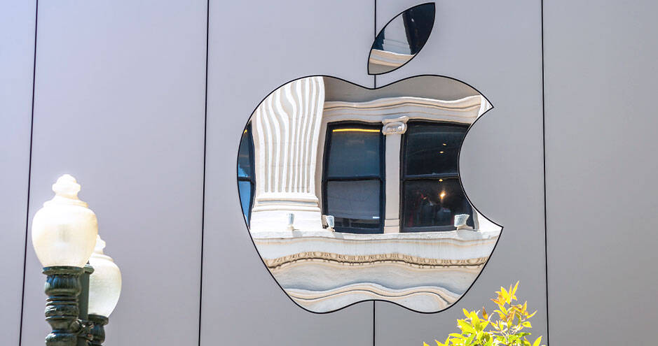 A reflective Apple logo on a building facade, distorting the reflection of classical architecture in its polished surface.