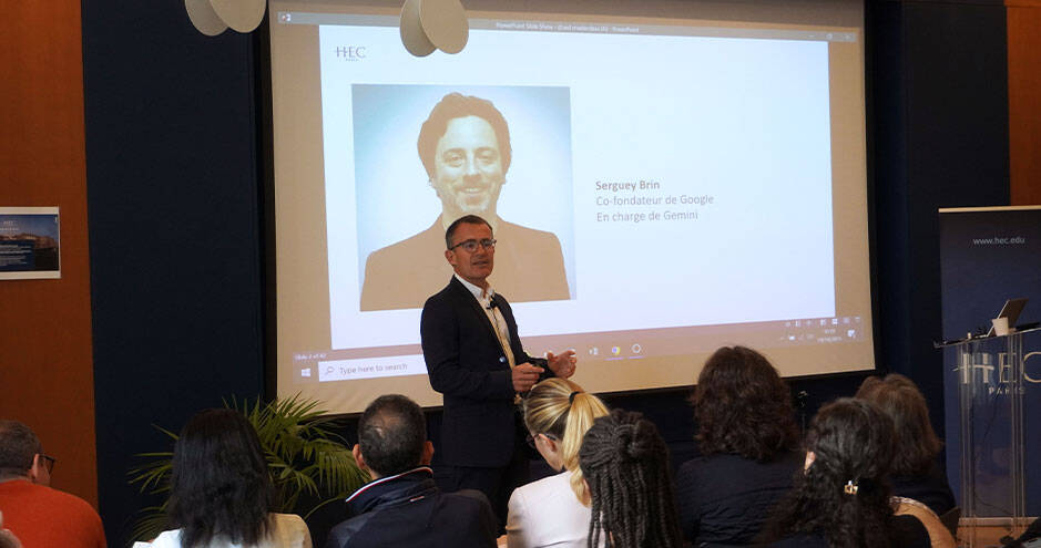 HEC Paris Professor presenting to an audience. A screen behind him displays a picture of Sergey Brin, co-founder of Google, in charge with Gemini