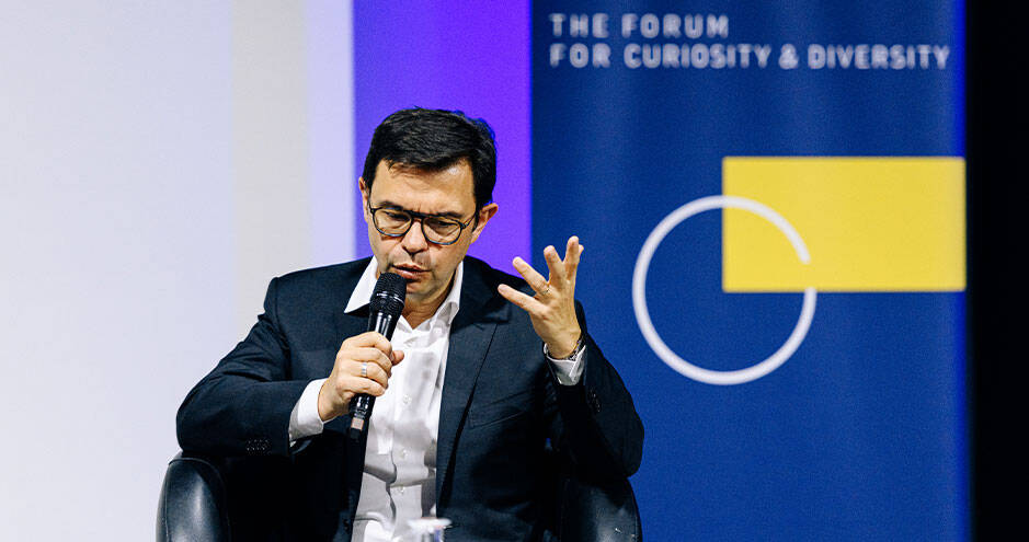 Rodolphe Durand, seated with a microphone, speaks and gestures during a panel discussion