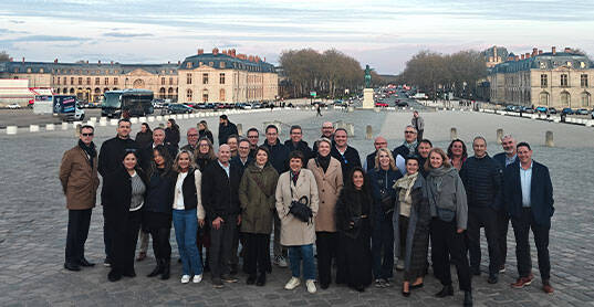 Around thirty participants pose as a group in front of the Château de Versailles.